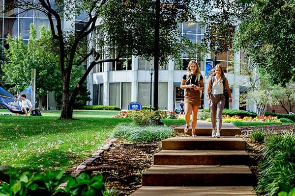 Two students walk in on a sidewalk on SLU's campus in front of Pius XII Memorial Library