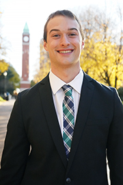 A headshot of Ben Kemper with a clocktower and trees in the background.