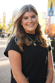 A headshot photo of Charlotte Schoen with a clocktower and trees in the background.