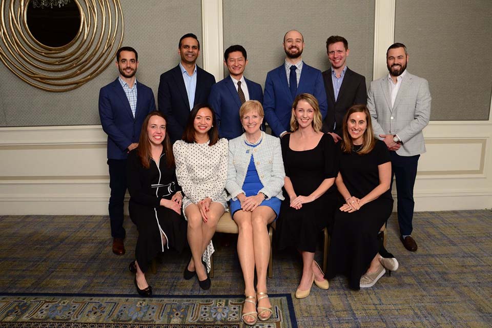 A group of alumni pose for a photo with the dean in a ballroom.