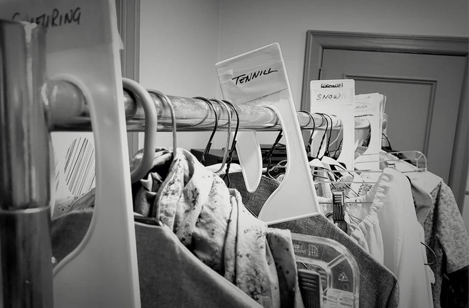 A black and white photo of a rack of costumes with a divider labeled "Tennill"