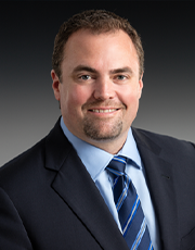 Headshot of Mark J. Brooks smiling for the camera and wearing a blue suit jacket and striped tie.