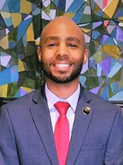 African American man smiling at the camera in a suit and tie against a colorful mosaic background