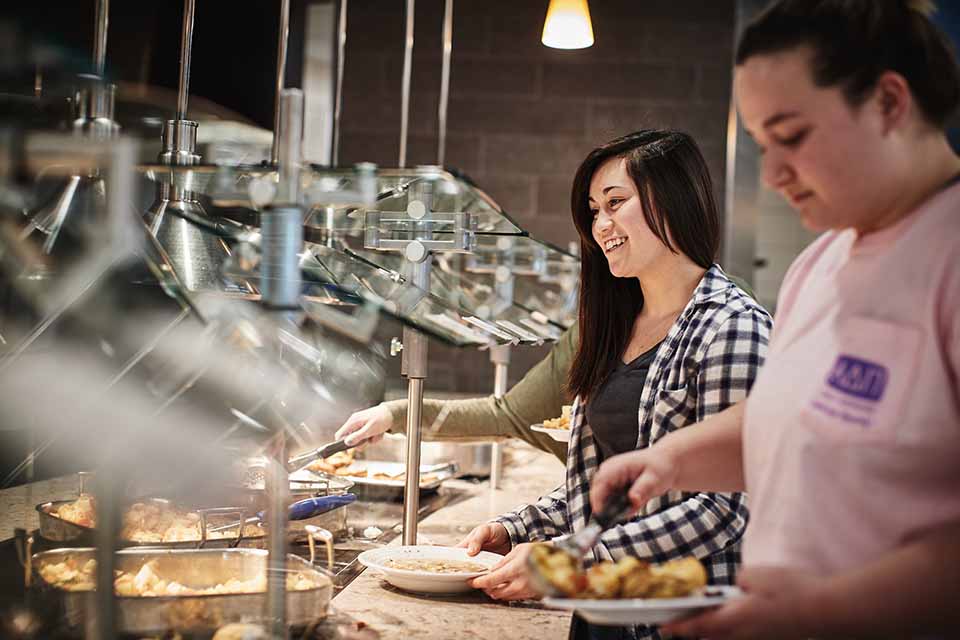 Two students dish food onto their plates in the dining hall.