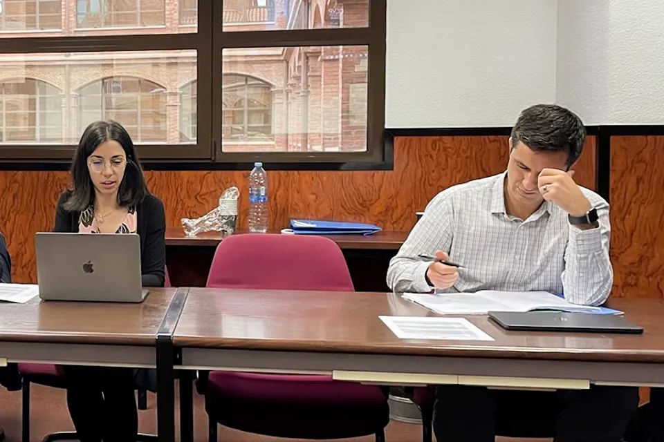 A woman and a man sitting at a table with laptops