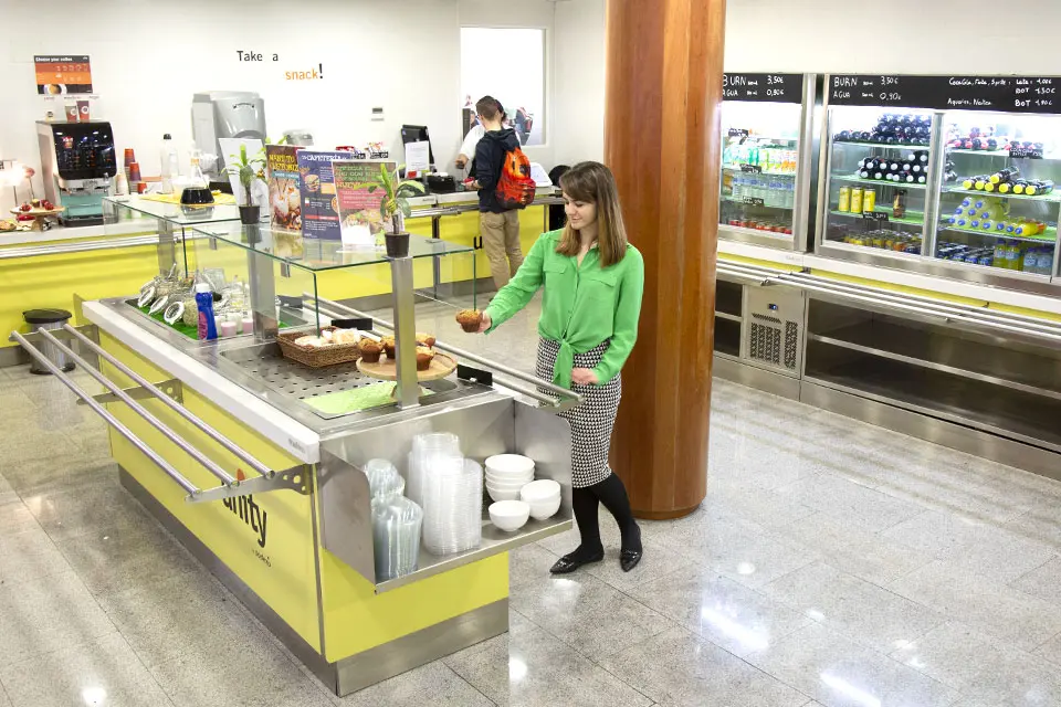 A customer selects a muffin from a selection of foods in a cafeteria.