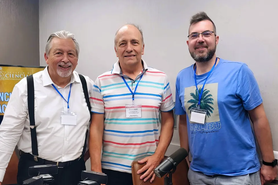 Profesor de SLU-Madrid participa en simposio internacional de cosmología en Chile Three men with lanyards pose for a picture looking into camera.