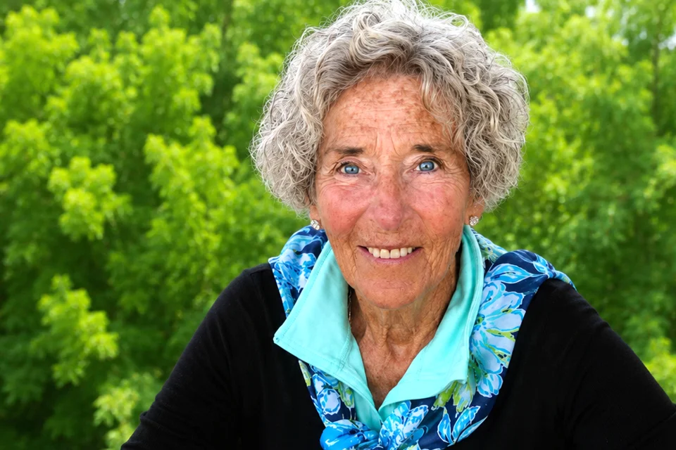 Linda Vogt portrait Portrait of Linda Vogt smiling outdoors, wearing a black top and blue scarf, with green trees in the background.