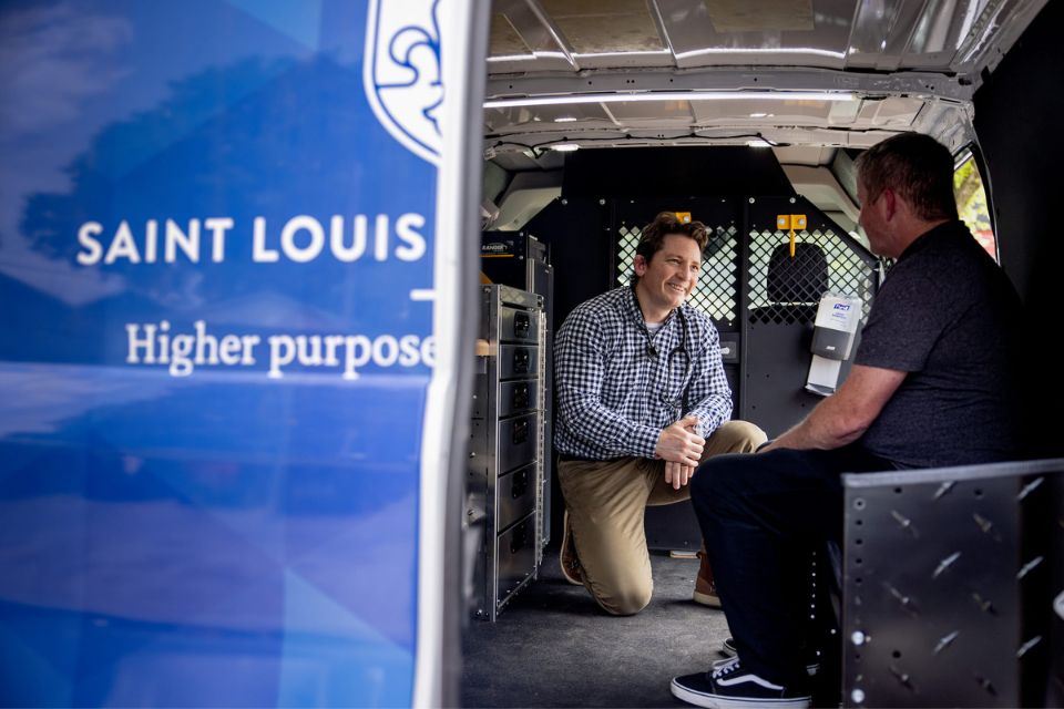 SLU Mobile Health Clinic A physicians kneels next to a patient sitting inside a mobile health clinic.