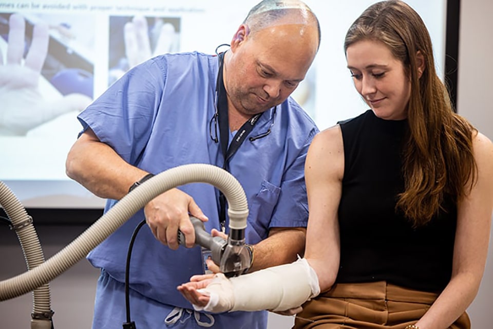 A nurse uses a tool to remove a cast from a woman's arm.