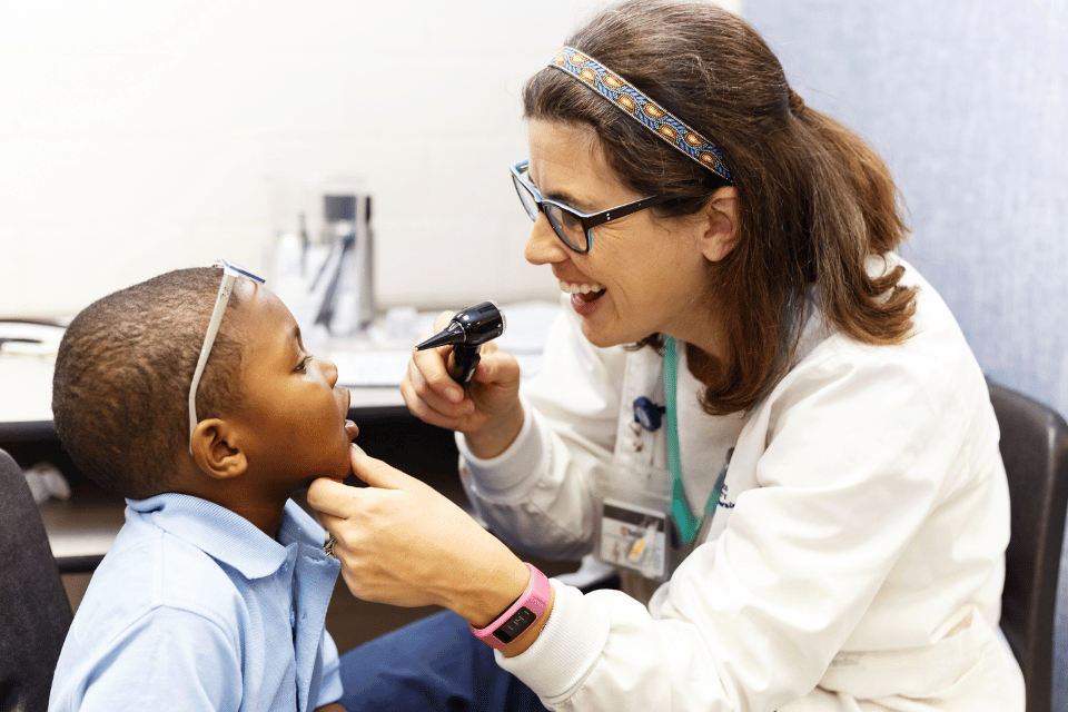 A nurse practitioner examining a young child's mouth and nose with an otoscope light.