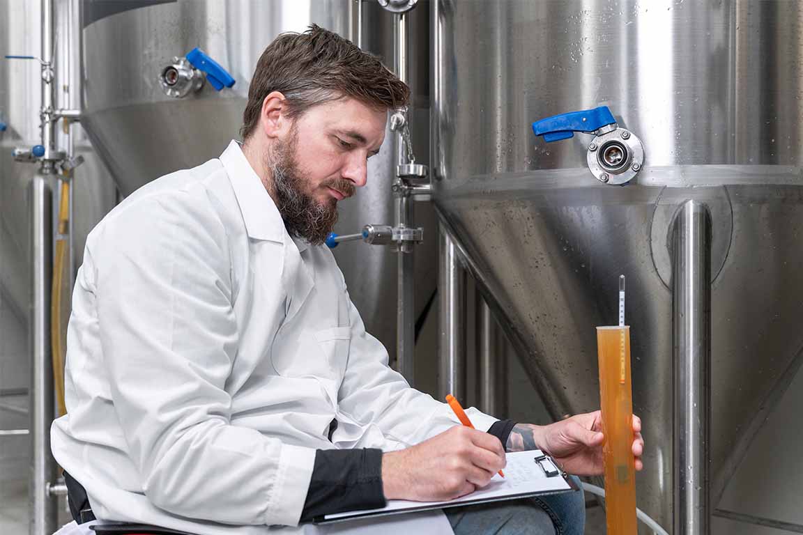 A man stands in front of a tank of beer writing on a clipboard