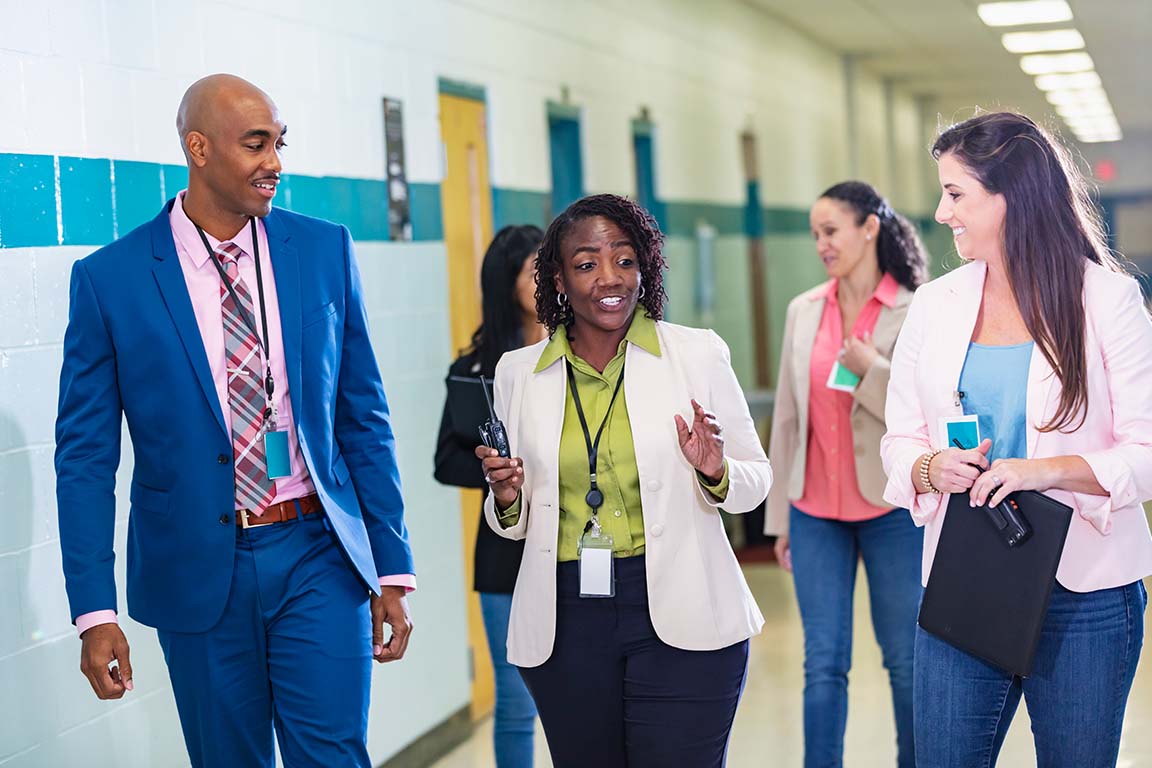 Three adults have a discussion in the hallway of a school. 