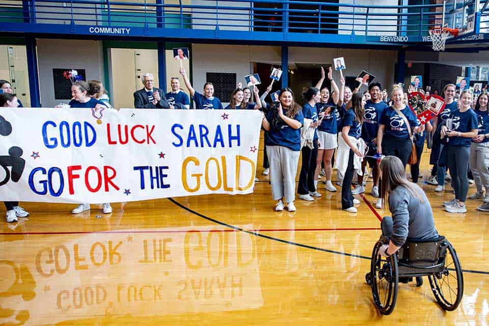 A large group of well-wishers present Sarah Adam with a banner that reads "Good luck, Sarah! Go for the gold!"